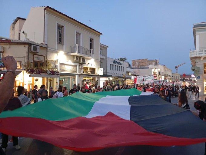 Crowds carrying an enormous Palestinian flag through the streets of Crete, as they march towards the port.