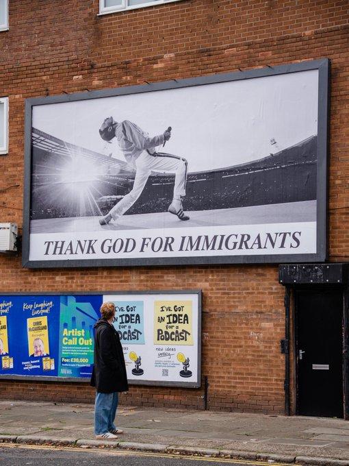 Black and white billboard on a brick wall in Liverpool shows Freddy Mercury on stage, with the caption THANK GOD FOR IMMIGRANTS