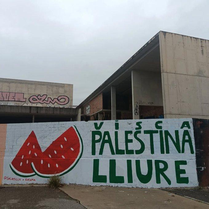 A white wall with two watermelon slices and VISCA PALESTINA LLIURE (LONG LIVE FREE PALESTINE) in green capitals
