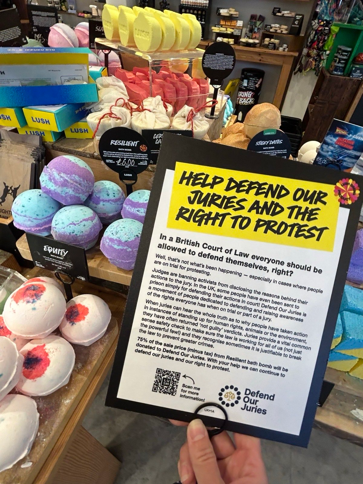Image of a counter at a branch of Lush, with a notice to advertise their new bath bomb reading: HELP DEFEND OUR JURIES AND THE RIGHT TO PROTEST