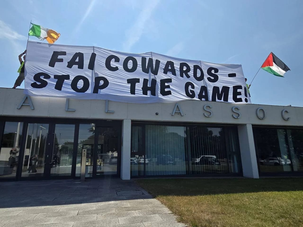 Picture of the FAI HQ with people on the roof holding a huge white banner reading FAI COWARDS STOP THE GAME.